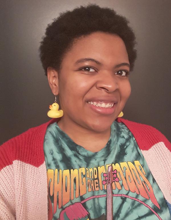 Woman with short hair in a pink sweater with rubber duck earrings smiling.