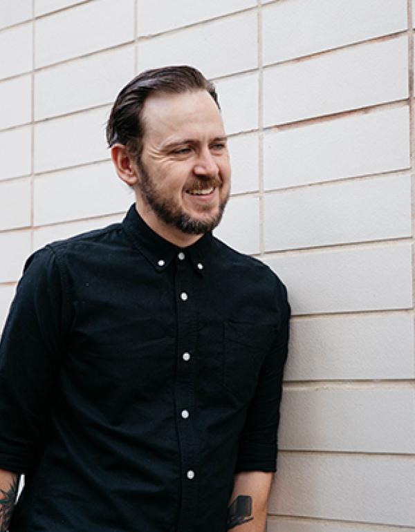 tony standing against a white wall smiling looking off camera