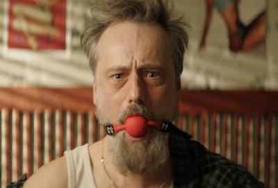 A man looks on with a ball gag in his mouth