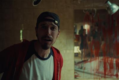 A guy looks scared with bloody mirror in the background