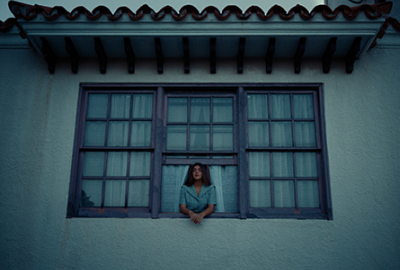 Naomi leaning out of a large window in her house