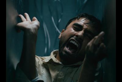 An Indian man screaming as two metal walls close in on either side of him.