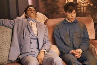 A man sits with a dead man on the couch