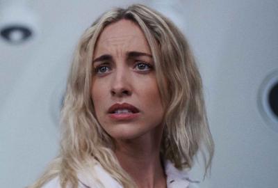 Woman with long blonde hair gazing offscreen in a stark, futuristic setting.